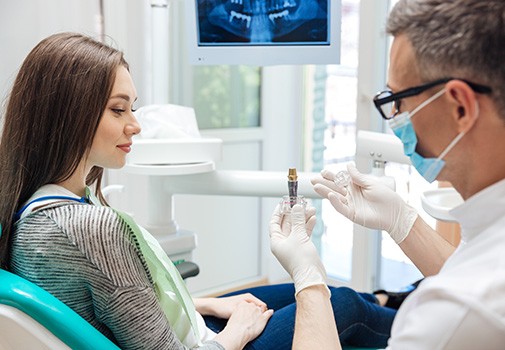 Dentist in white gloves showing sample implant to patient in dental chair