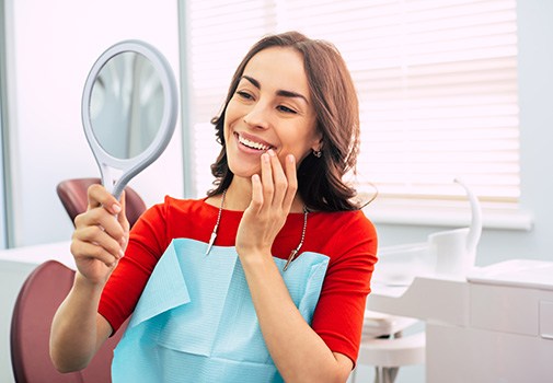 Woman in red-orange shirt admiring smile in dental office
