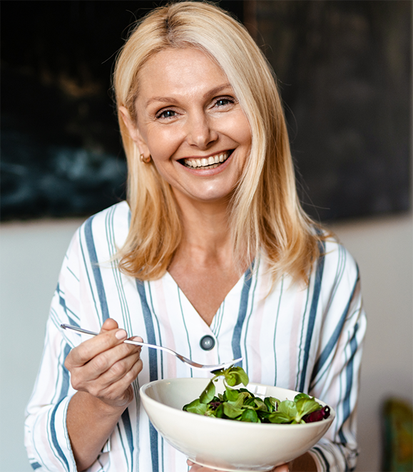 Woman eating a salad and smiling with dental implants in Medford