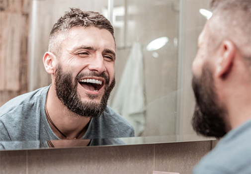 Bearded man smiling in front of a mirror