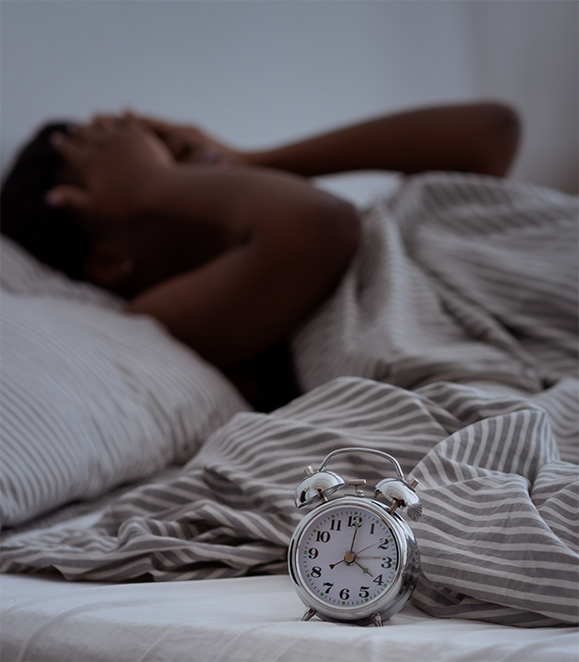 Person in bed rubbing their eyes with a nightstand clock showing 4 in the morning